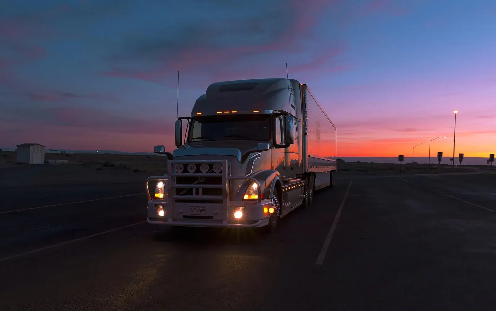Semi truck parked at a highway rest area at dusk under a purple sky