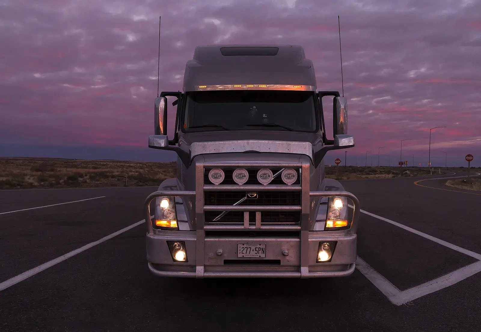 Front of a long-haul semi truck with its lights on at dusk